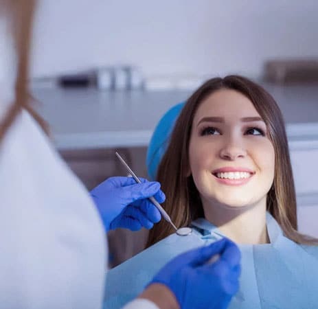 Young woman smiling in dental chair during examination with dentist in blue gloves.