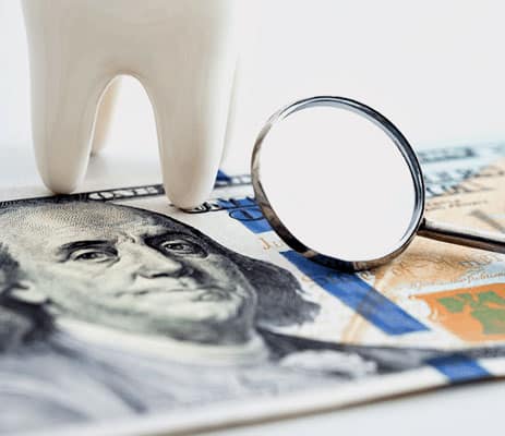 Dental mirror and tooth model on scattered dollar bills and credit cards, depicting dental costs.