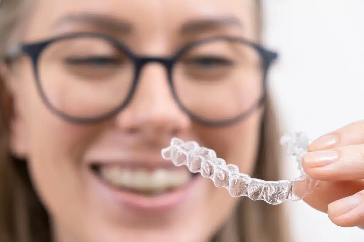 A person smiling confidently and holding a clear Invisalign aligner.